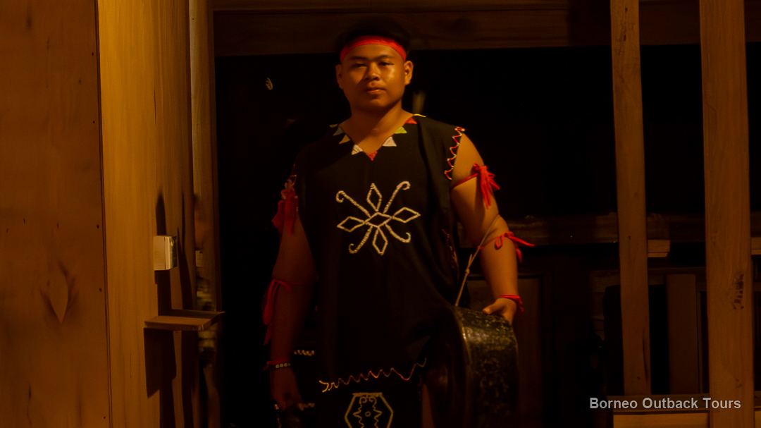 Murut man in a traditional black warrior jacket holding a gong inside a longhouse in Sapulot, Sabah
